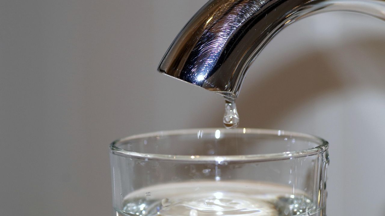 Wassertropfen fällt aus einem Hahn in ein Glas