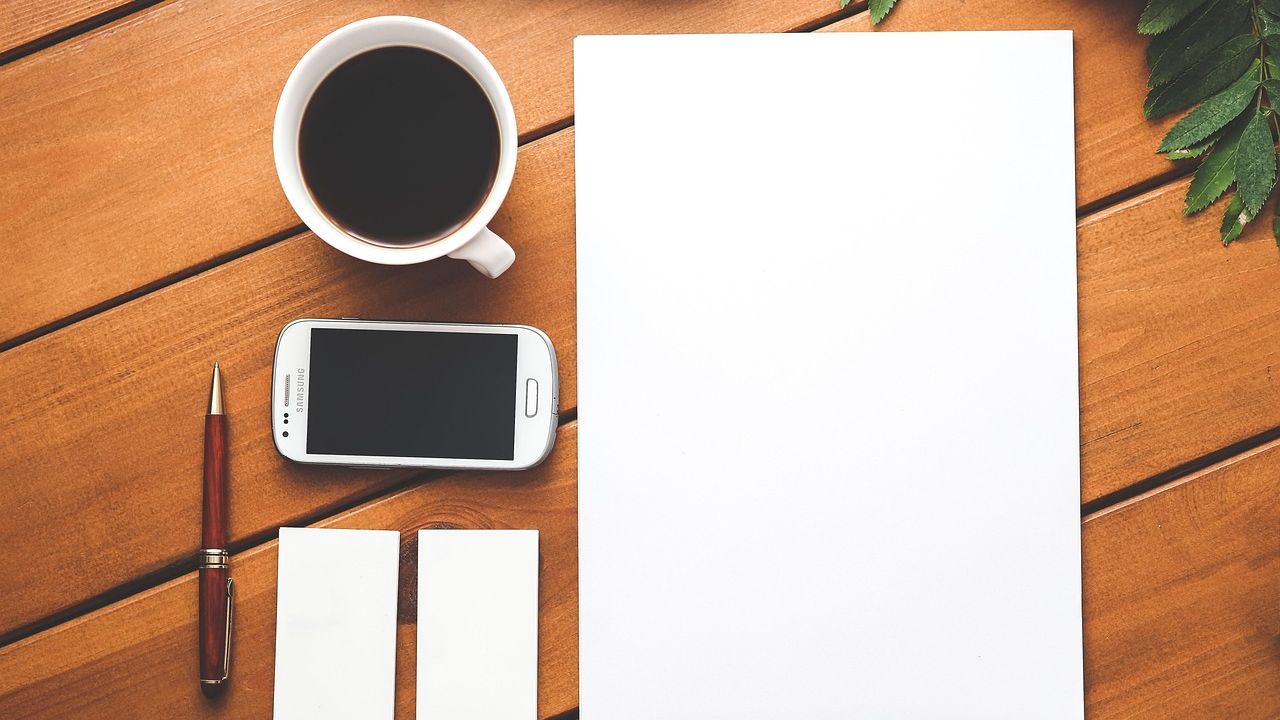 Smartphone, Kaffeetasse und Notizpapier auf einem Holztisch